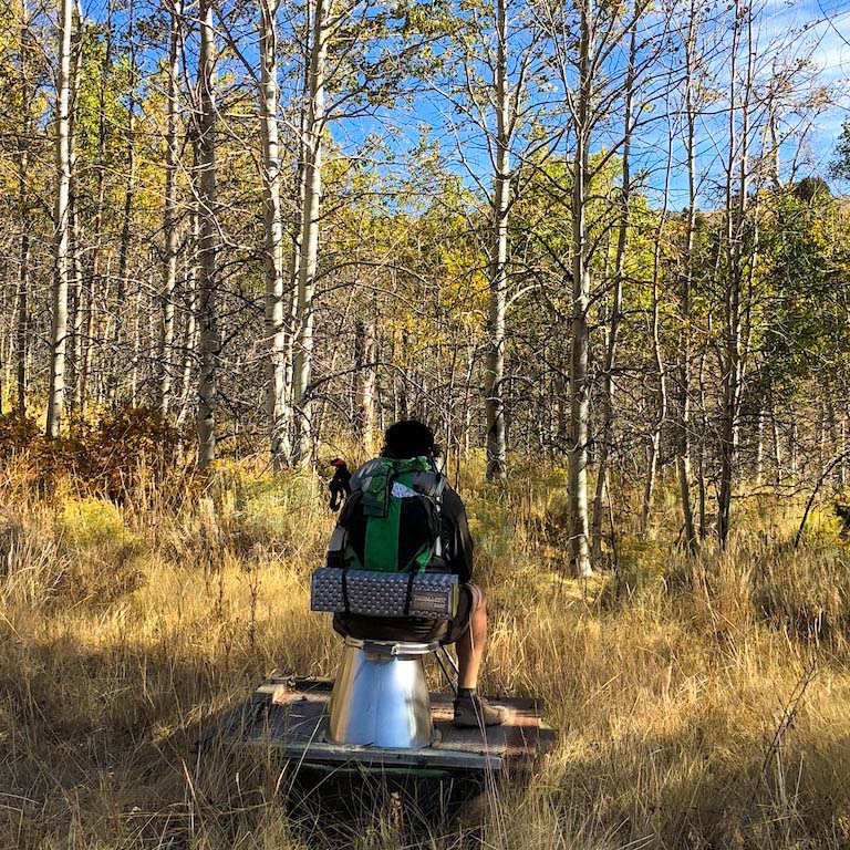 A hiker sitting on an open air outhouse in hart mountain wildlife area