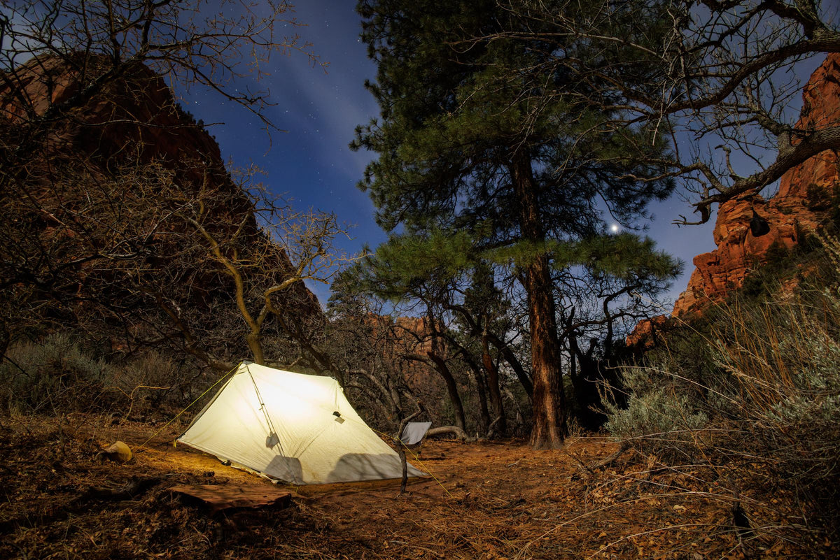 Haven tent glowing at night in a Utah canyon beneath red rock walls and a ponderosa pine