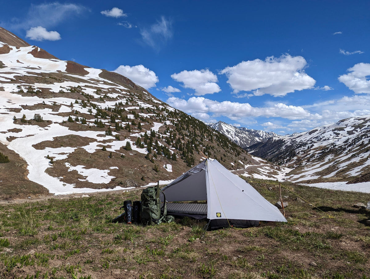 Gray Haven tent pitched in a green alpine valley below snowfields and peaks