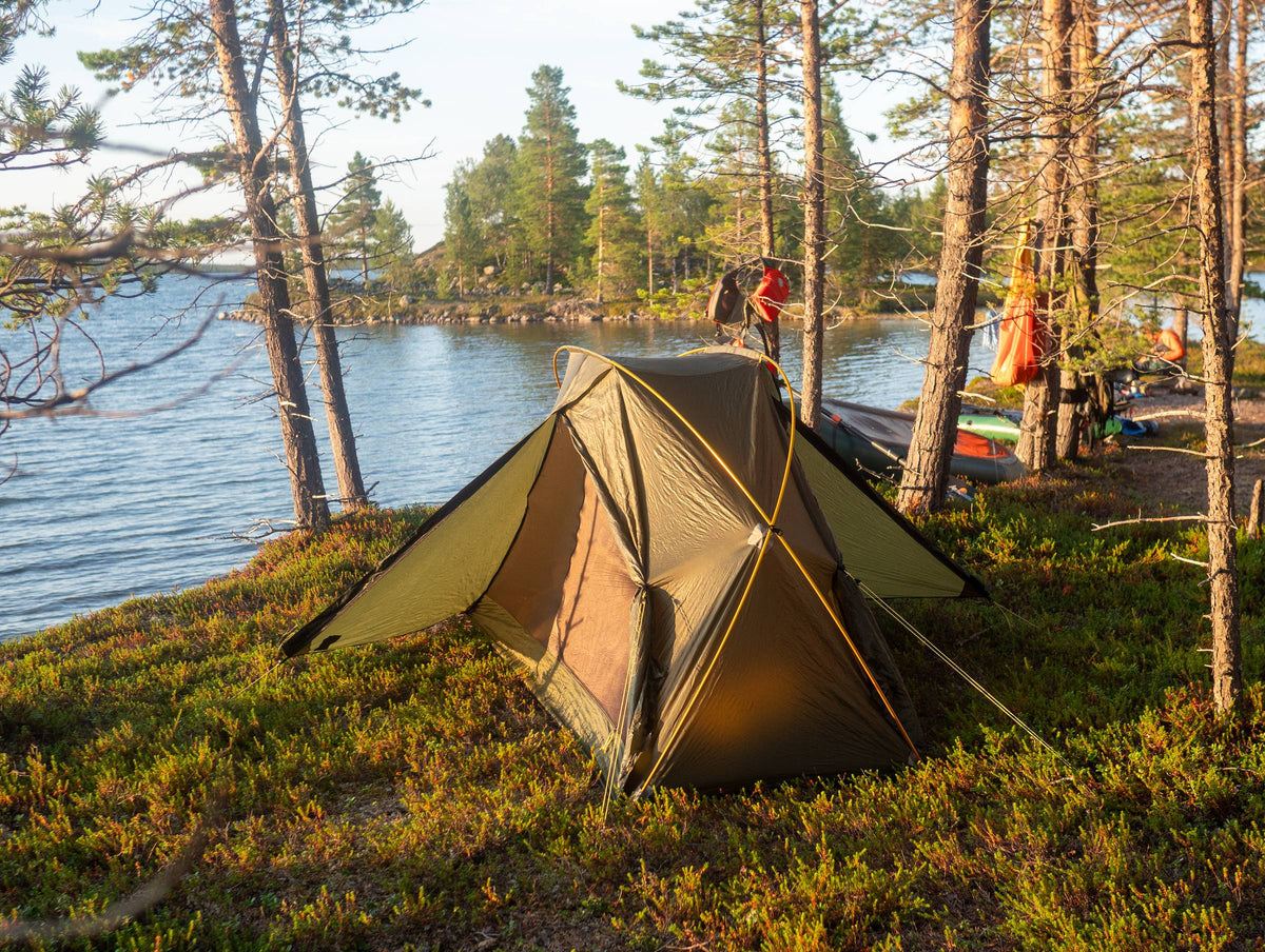 Lunar Orbiter tent pitched on a grassy lakeshore among pines in warm evening light