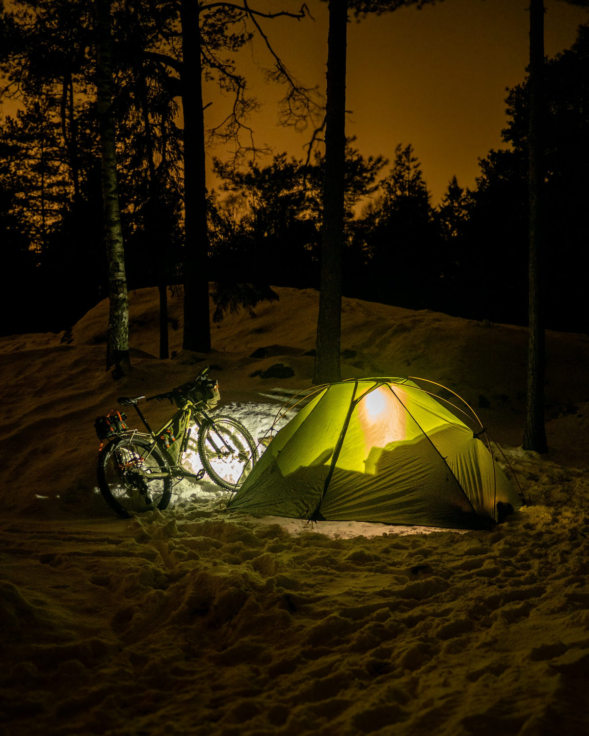 Lunar Orbiter glowing at night in a snowy forest next to a fat bike