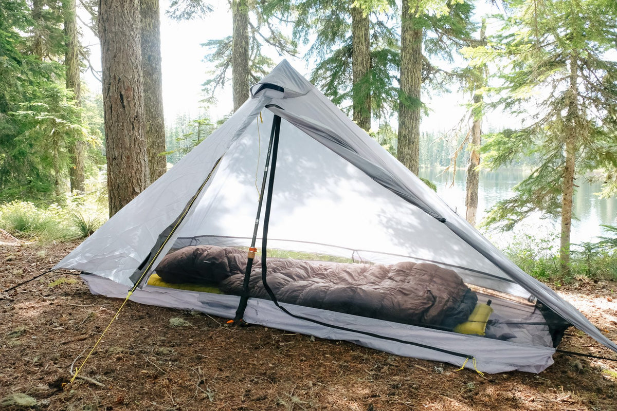 Gray Lunar Solo with the door open and a sleeping bag inside, pitched in a lakeside forest