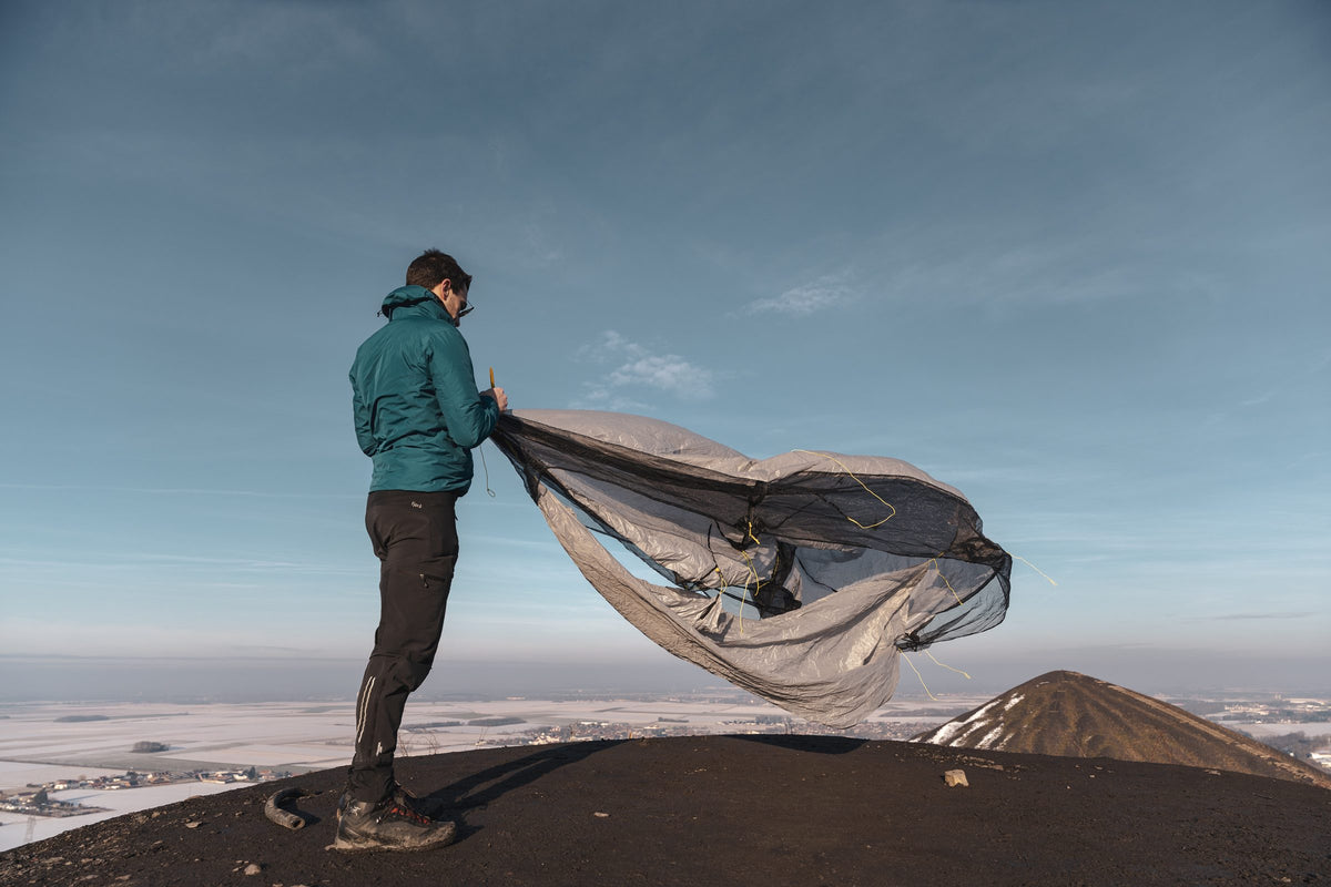 Hiker unfurling the Owyhee tarp in the wind on a volcanic summit above the clouds