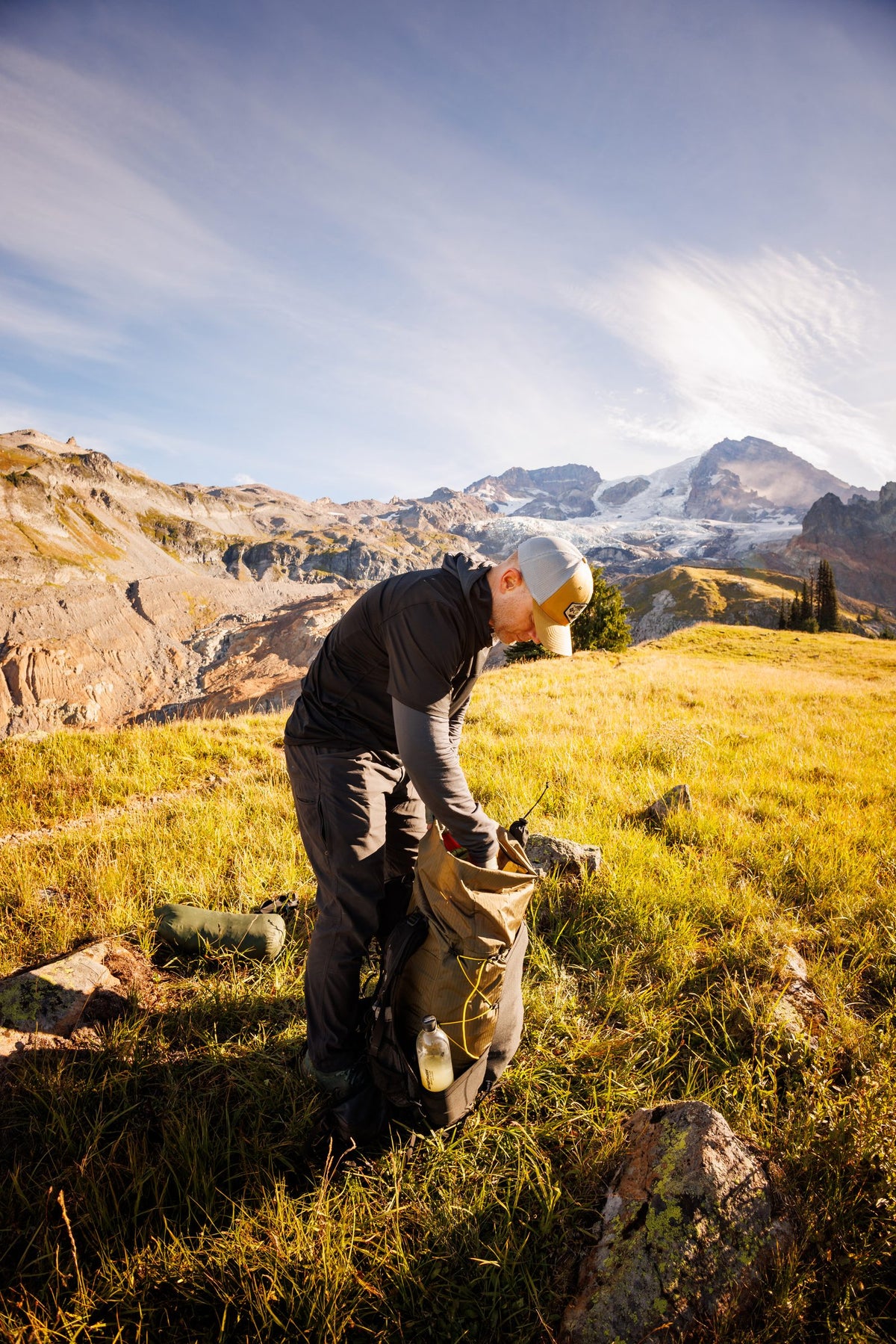 Hiker packing a backpack lined with the Pack Liner in a golden alpine meadow near Mount Rainier