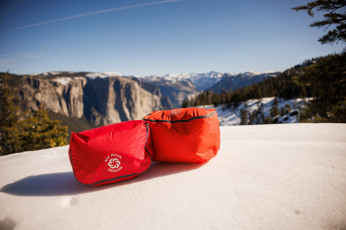 Two red packing pods on a snowy ledge overlooking Yosemite Valley