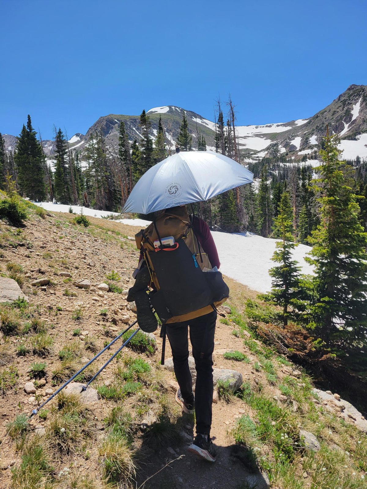 Hiker on a mountain trail with a Silver Shadow Carbon umbrella mounted hands-free on their pack