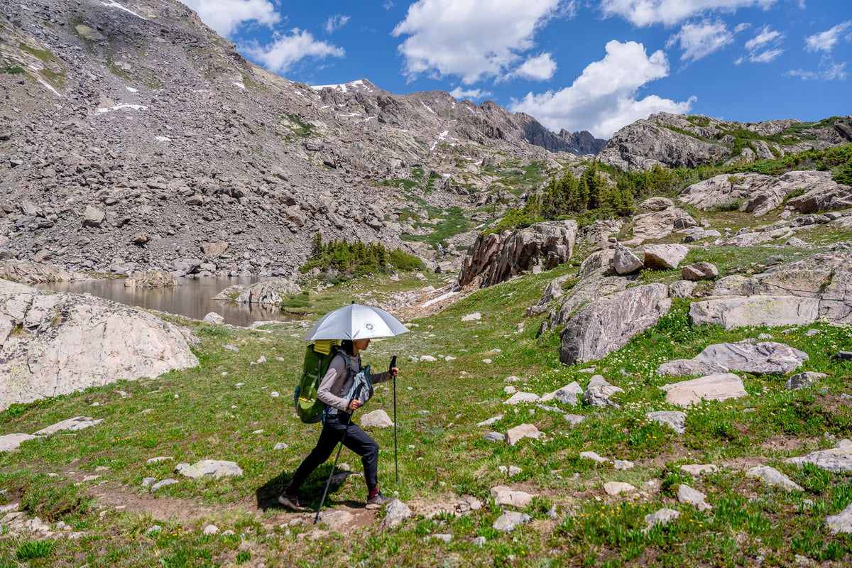 Hiker walking an alpine trail under a Silver Shadow umbrella with a lake behind