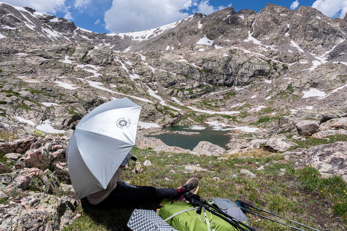 Hiker resting in the shade of a Silver Shadow umbrella above an alpine lake