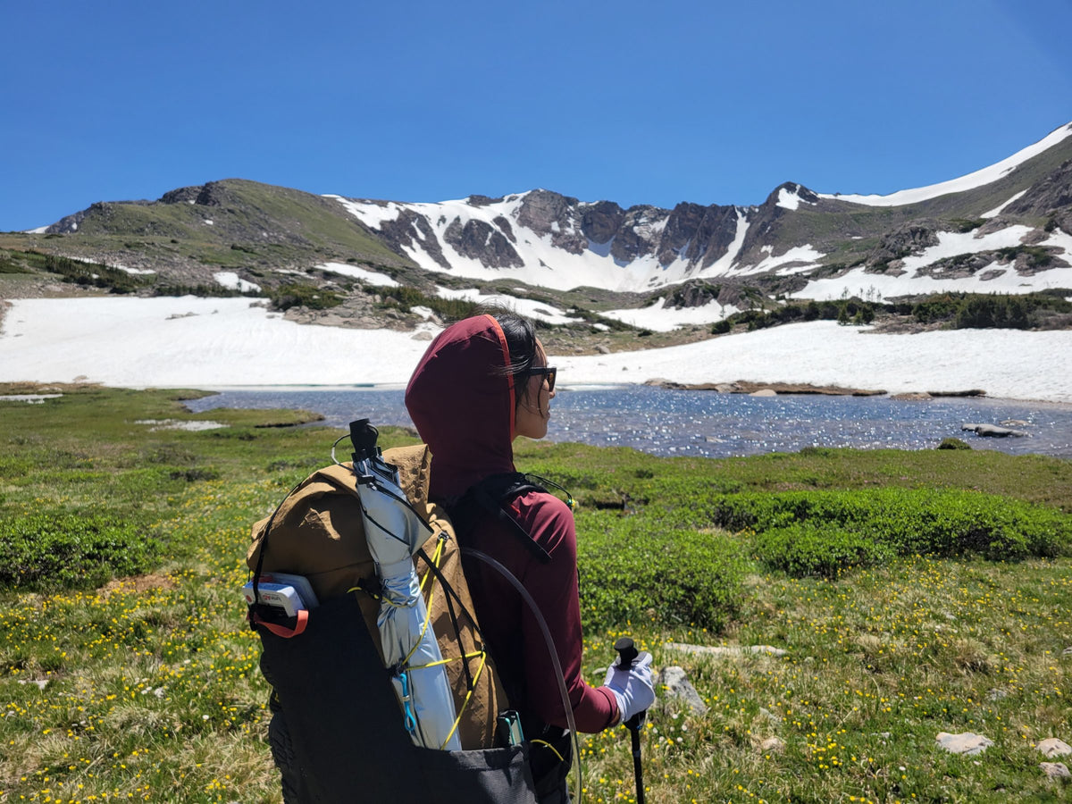 Hiker with a Silver Shadow umbrella stowed on their backpack beside a snowy alpine lake