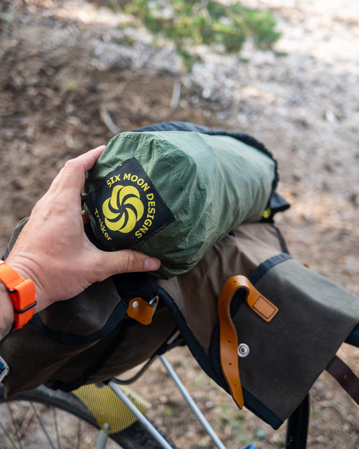 Hand holding the packed Skyscape Trekker stuff sack on a bikepacking handlebar bag