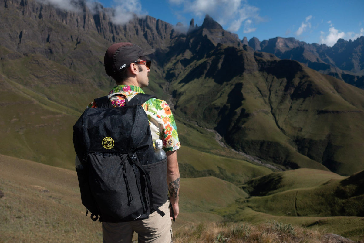 Hiker with a black Wy'east daypack overlooking green mountain ridges in South Africa