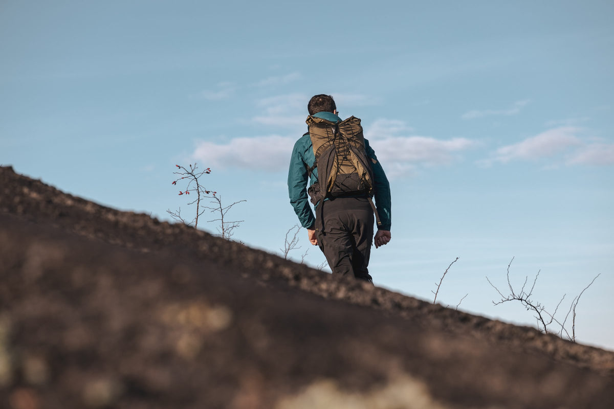 Hiker with a coyote Flight 30 backpack walking a volcanic slope against a blue sky