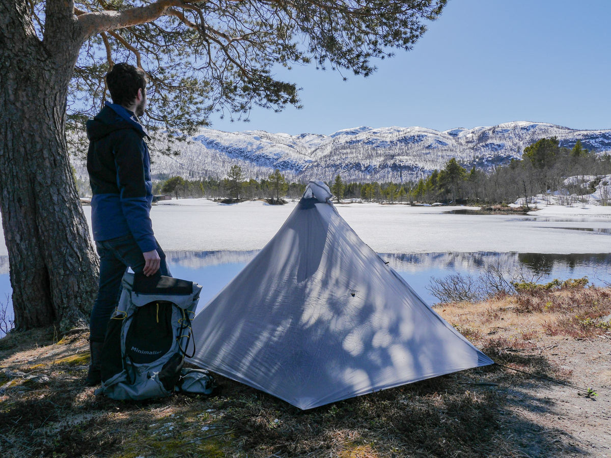 Hiker beside a gray Gatewood Cape pitched at a snowy lakeshore near Geilo, Norway