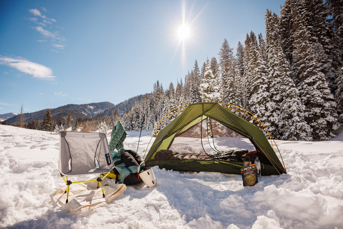 Green Lunar Orbiter tent with the door open at a sunny snow camp in a Utah pine forest