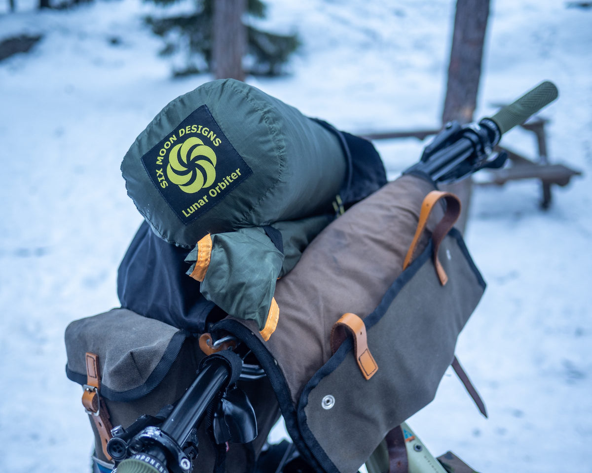 Packed Lunar Orbiter stuff sack strapped to a bikepacking handlebar roll in the snow