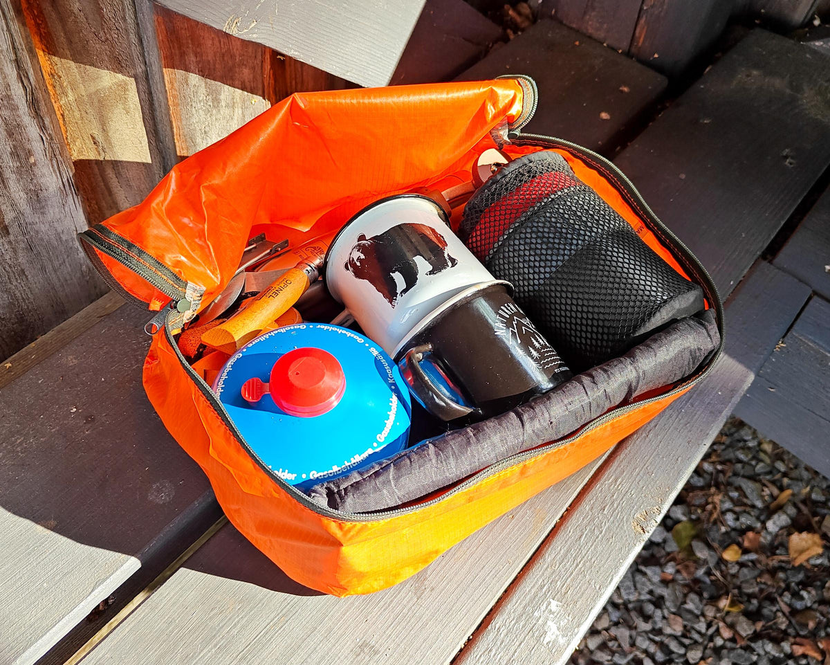Open orange packing pod holding a cook kit with mug, stove and fuel canister