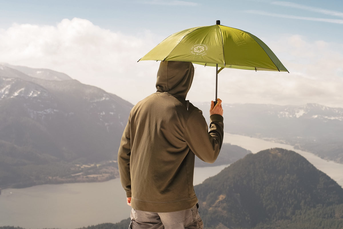 Hiker in a hood holding an olive Rain Walker SUL umbrella above a river gorge