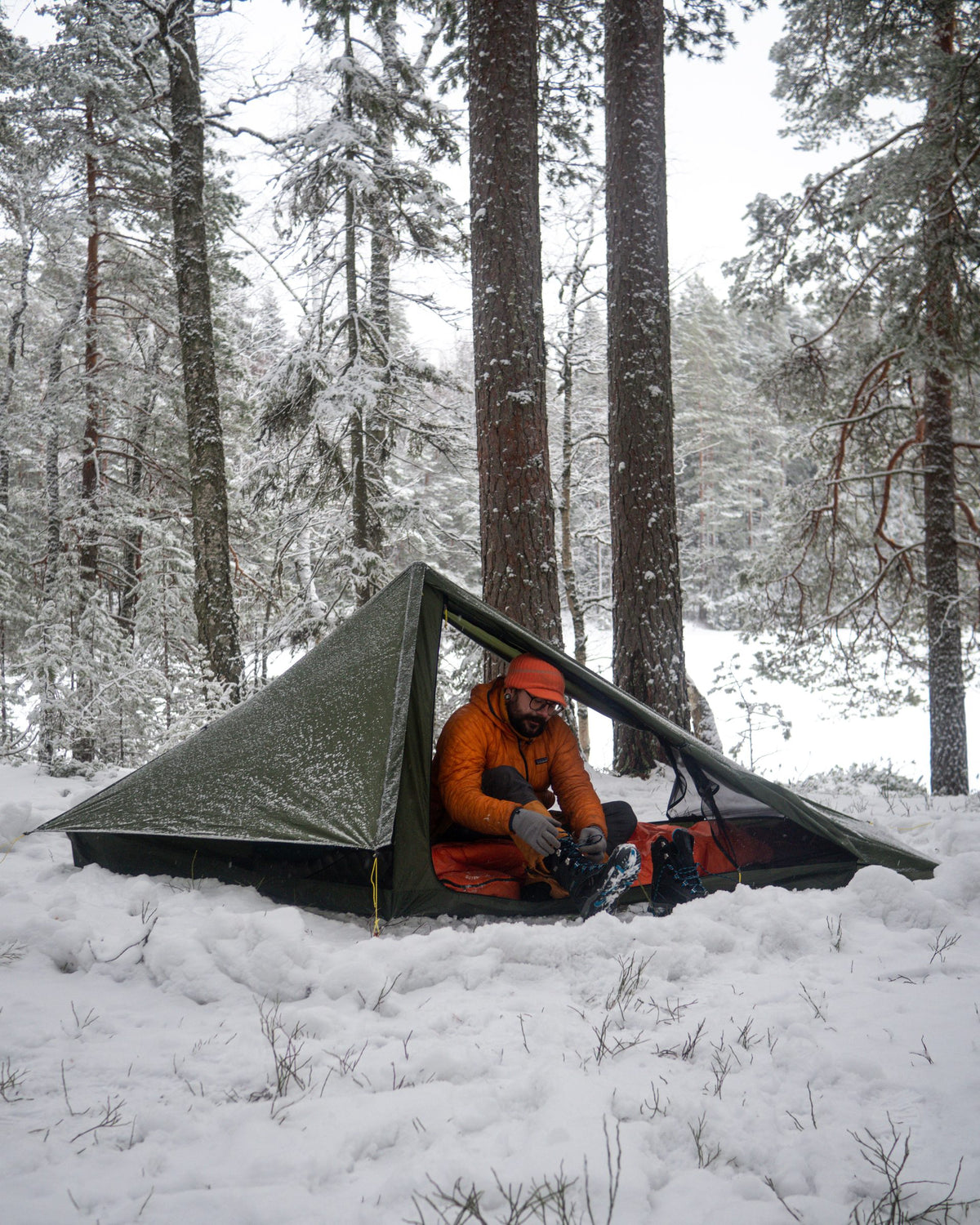 Camper in an orange jacket sitting in the door of a Skyscape Trekker in a snowy forest