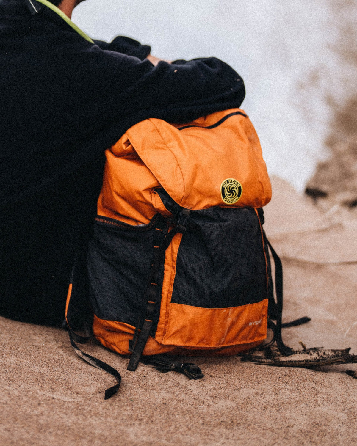 Orange and black Wy'east daypack sitting on sand next to a hiker