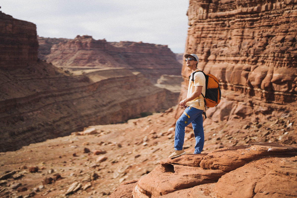 Hiker with an orange Wy'east daypack standing on a red sandstone canyon ledge