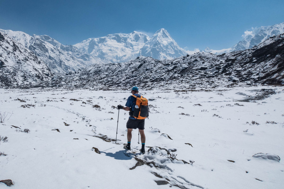 Hiker with an orange Wy'east daypack crossing a snowfield toward high snowy peaks